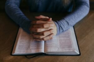 Mãos entrelaçadas em oração sobre uma Bíblia Sagrada aberta em momento de fé e reflexão espiritual - Minutos de Paz
